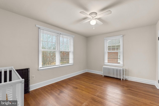 unfurnished bedroom featuring radiator, ceiling fan, multiple windows, and hardwood / wood-style flooring