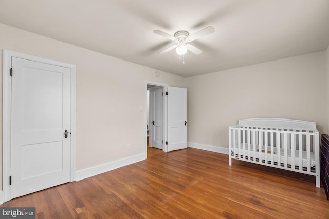 unfurnished bedroom featuring ceiling fan, hardwood / wood-style floors, and a nursery area