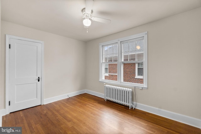 empty room with hardwood / wood-style floors, ceiling fan, and radiator heating unit