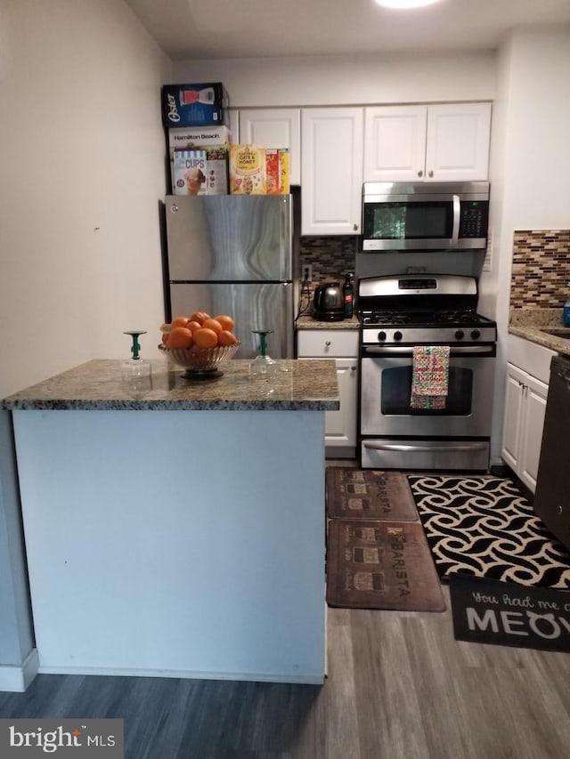 kitchen featuring decorative backsplash, dark stone countertops, appliances with stainless steel finishes, dark hardwood / wood-style flooring, and white cabinetry