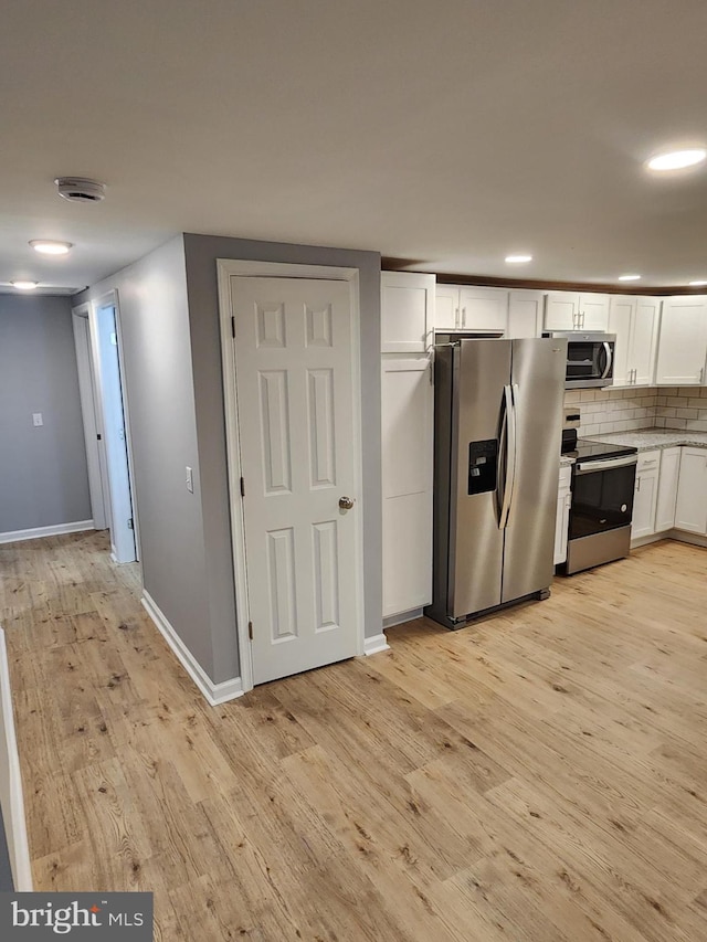 kitchen with backsplash, white cabinetry, light wood-type flooring, and appliances with stainless steel finishes