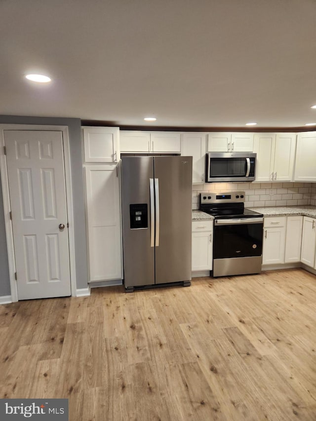 kitchen with white cabinets, decorative backsplash, light stone countertops, appliances with stainless steel finishes, and light hardwood / wood-style floors