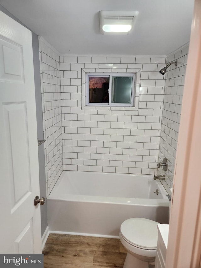 bathroom with hardwood / wood-style flooring, tiled shower / bath combo, and toilet