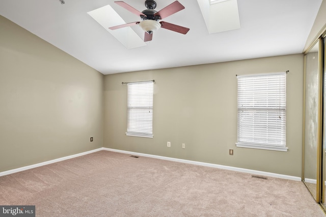 spare room with light colored carpet, lofted ceiling with skylight, and ceiling fan