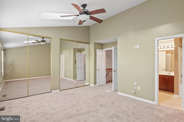 unfurnished bedroom featuring ensuite bath, light carpet, ceiling fan, and two closets