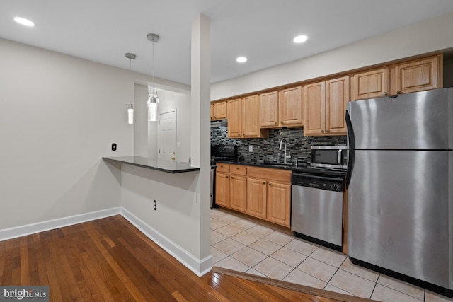 kitchen with pendant lighting, sink, decorative backsplash, light wood-type flooring, and appliances with stainless steel finishes