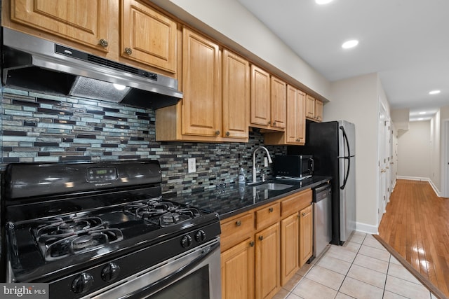 kitchen with sink, stainless steel appliances, backsplash, dark stone countertops, and light tile patterned flooring