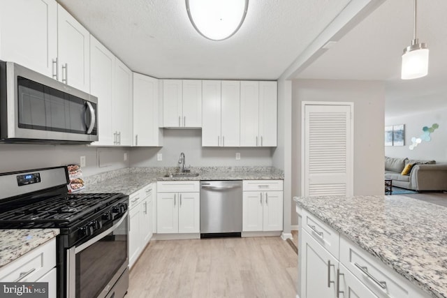 kitchen featuring white cabinets, sink, appliances with stainless steel finishes, decorative light fixtures, and light hardwood / wood-style floors