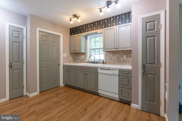 kitchen with light wood-type flooring, tasteful backsplash, gray cabinetry, white dishwasher, and sink