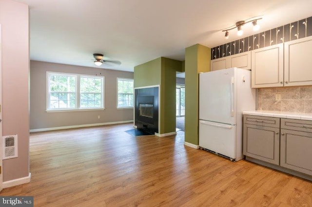 kitchen featuring light wood-type flooring, tasteful backsplash, ceiling fan, white fridge, and a wood stove