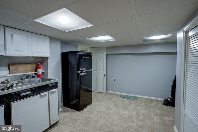 kitchen with a drop ceiling, stainless steel gas cooktop, light colored carpet, black refrigerator, and white cabinets