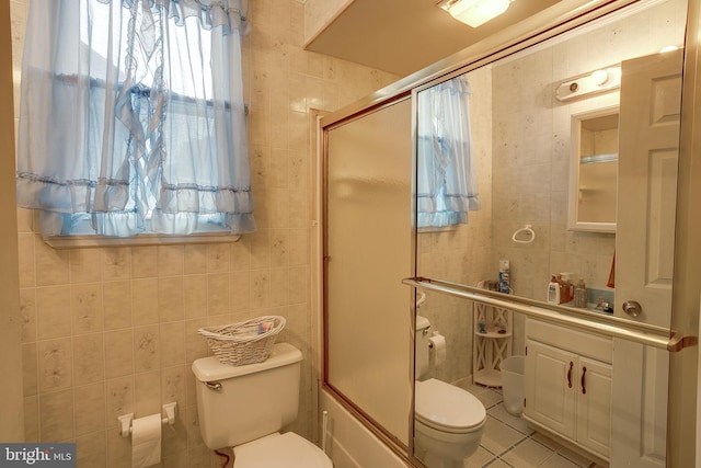 bathroom featuring tile patterned floors, toilet, bath / shower combo with glass door, and tile walls