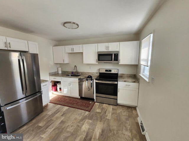 kitchen featuring stainless steel appliances, a sink, white cabinetry, and light wood-style floors