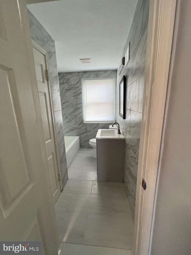 bathroom featuring a tub, tile patterned flooring, toilet, vanity, and tile walls