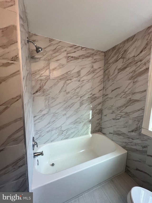 bathroom with tiled shower / bath, toilet, and tile walls