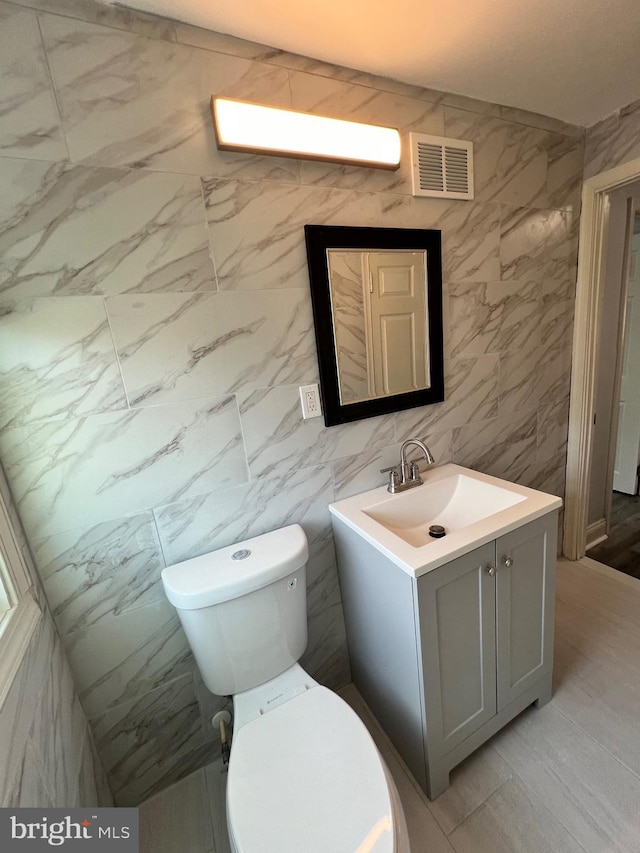 bathroom with vanity, toilet, and tile walls