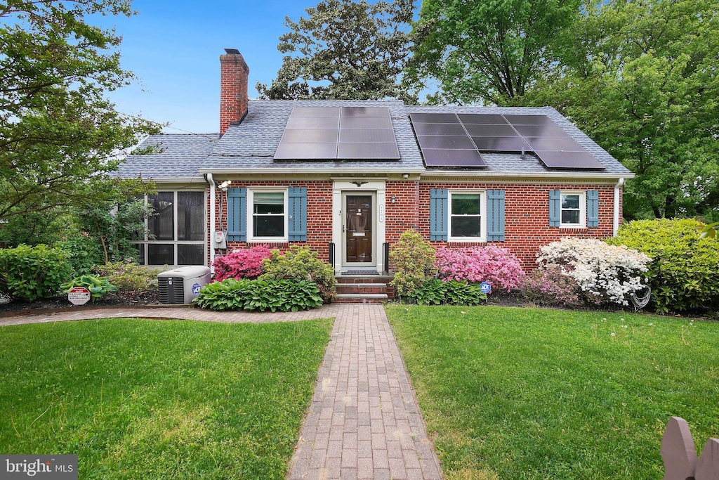 view of front of home with solar panels, cooling unit, and a front lawn