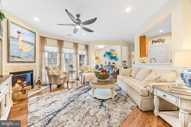 living room with ceiling fan, a fireplace, and light hardwood / wood-style flooring