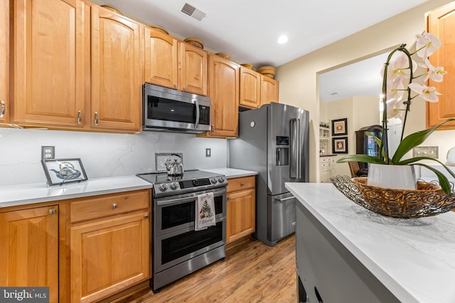 kitchen with backsplash, stainless steel appliances, and light wood-type flooring