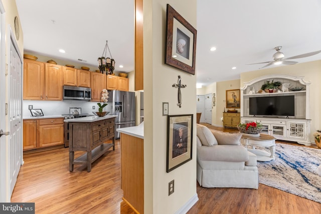 kitchen featuring a kitchen breakfast bar, stainless steel appliances, ceiling fan, light hardwood / wood-style floors, and a kitchen island