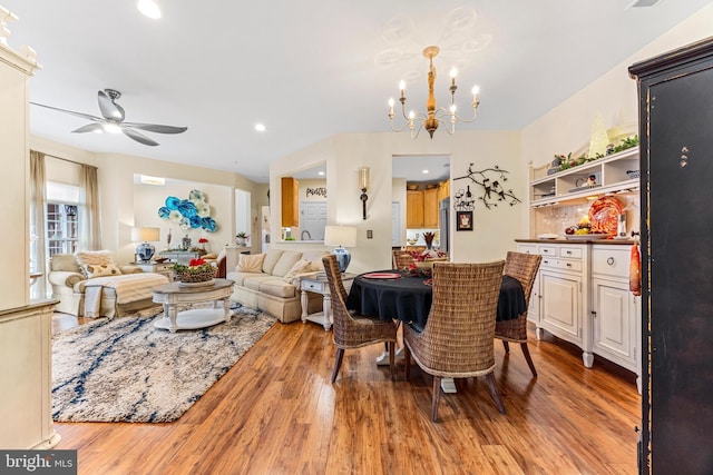 dining area with ceiling fan with notable chandelier and light hardwood / wood-style floors