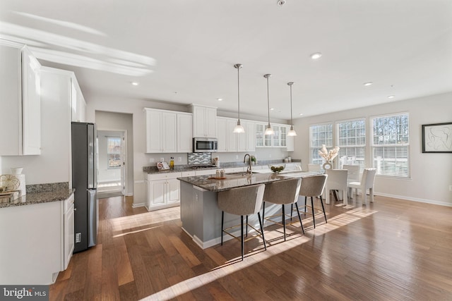 kitchen featuring dark stone counters, white cabinetry, a center island with sink, and stainless steel appliances