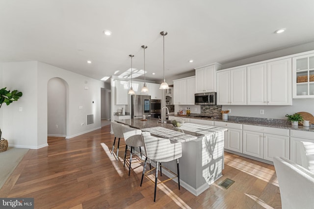 kitchen featuring a kitchen breakfast bar, stainless steel appliances, stone counters, white cabinets, and an island with sink