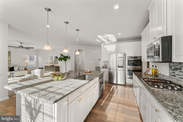 kitchen featuring sink, backsplash, a kitchen island with sink, white cabinets, and appliances with stainless steel finishes