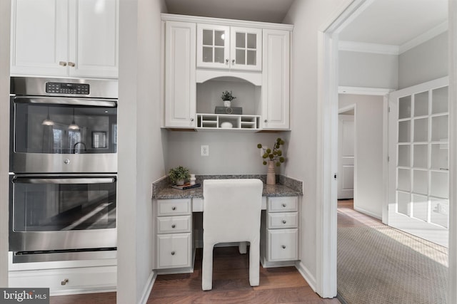 kitchen featuring dark colored carpet, double oven, dark stone counters, white cabinets, and built in desk