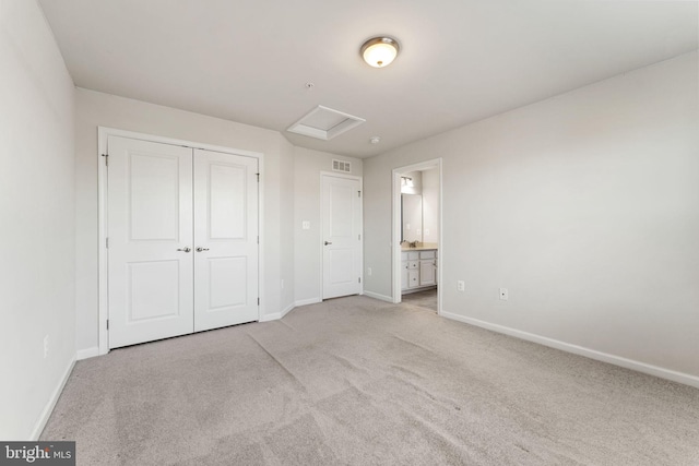 unfurnished bedroom featuring ensuite bathroom, a closet, and light colored carpet