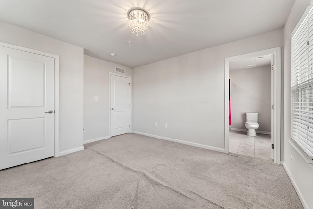 unfurnished bedroom with ensuite bathroom, light colored carpet, and an inviting chandelier