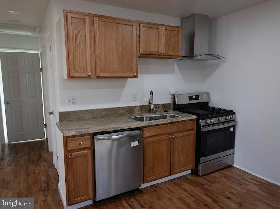 kitchen featuring appliances with stainless steel finishes, dark hardwood / wood-style flooring, wall chimney exhaust hood, and sink