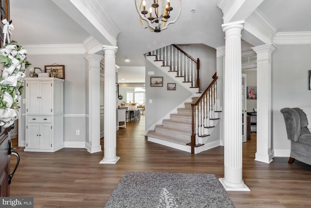 foyer entrance featuring a chandelier, ornamental molding, ornate columns, and dark wood-type flooring