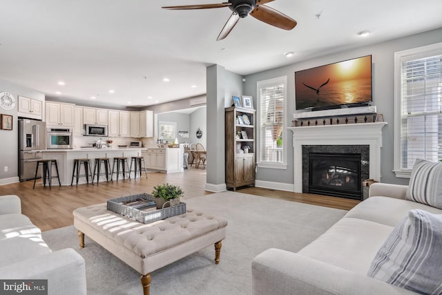 living room featuring ceiling fan, sink, a high end fireplace, and light wood-type flooring