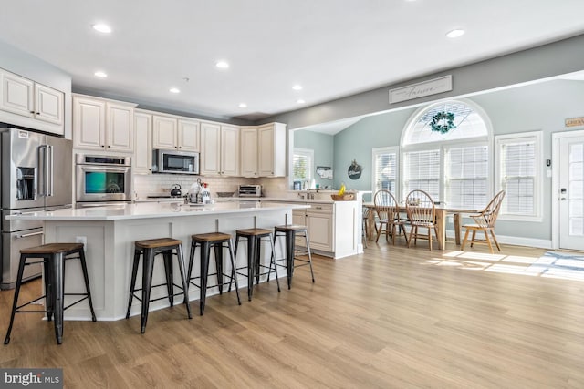 kitchen with light hardwood / wood-style floors, a kitchen bar, a kitchen island, and appliances with stainless steel finishes