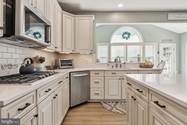 kitchen featuring decorative backsplash, appliances with stainless steel finishes, vaulted ceiling, sink, and light hardwood / wood-style floors