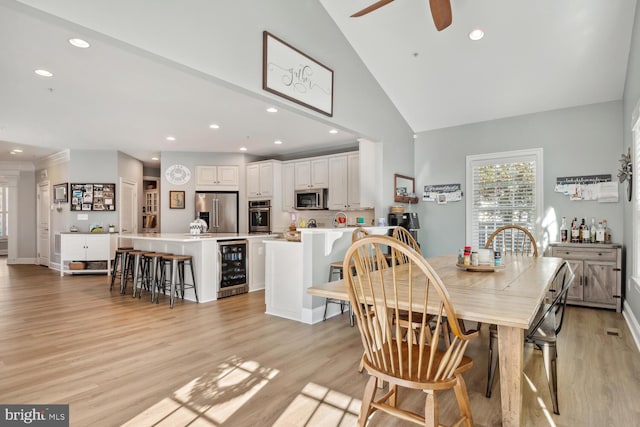 dining area with light hardwood / wood-style floors, high vaulted ceiling, beverage cooler, and ceiling fan