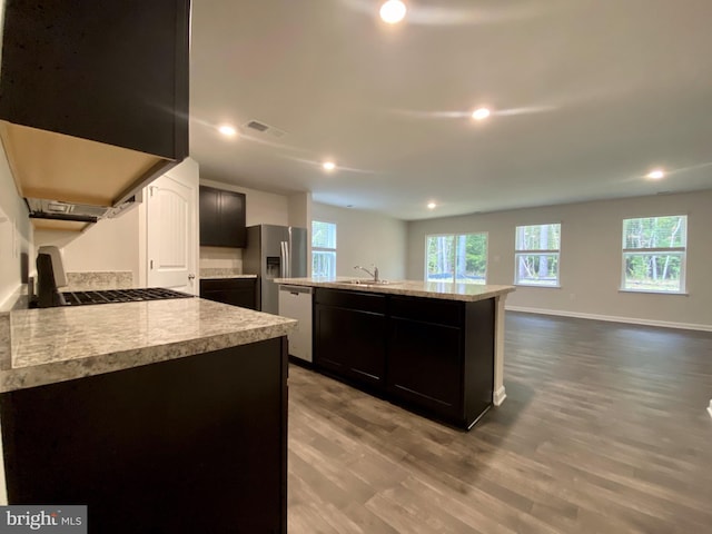 kitchen with a kitchen island with sink, sink, hardwood / wood-style flooring, light stone counters, and stainless steel appliances