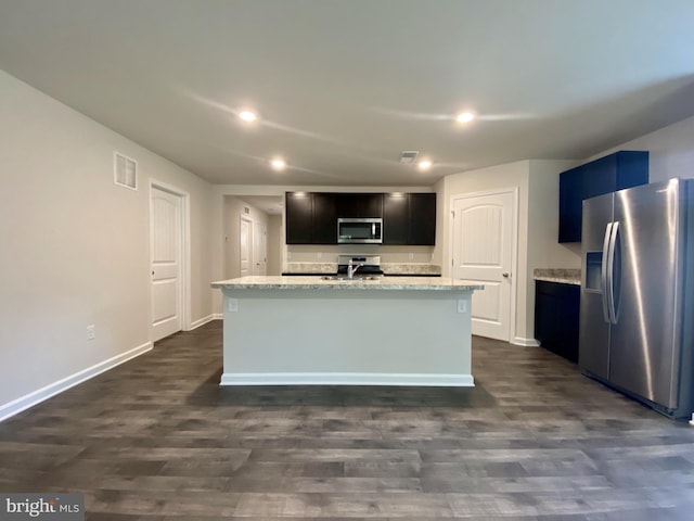 kitchen with light stone countertops, dark hardwood / wood-style flooring, an island with sink, and stainless steel appliances