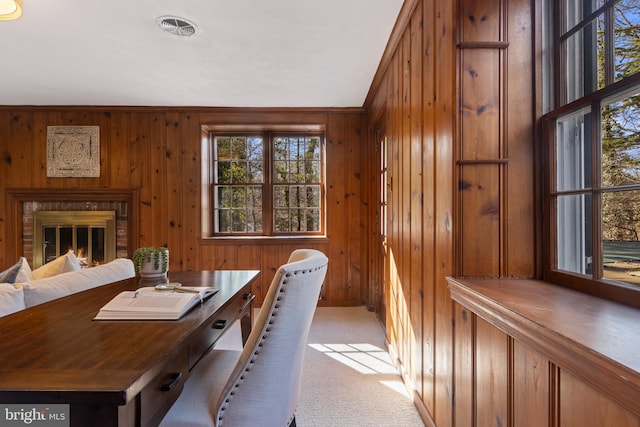 home office with wooden walls, a brick fireplace, and light carpet