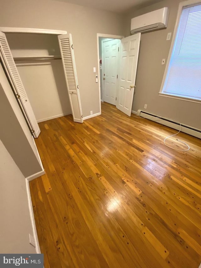 unfurnished bedroom featuring multiple windows, hardwood / wood-style flooring, an AC wall unit, and baseboard heating