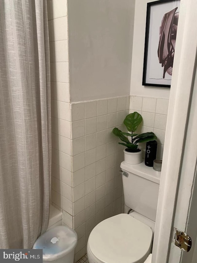 bathroom with a shower with shower curtain, toilet, and tile walls