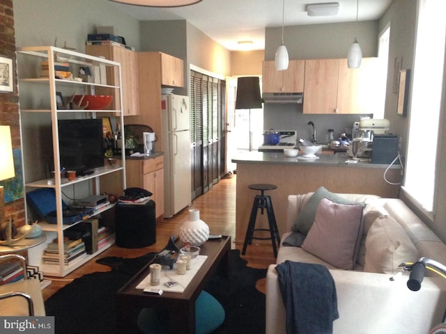 kitchen featuring light wood-type flooring, light brown cabinetry, decorative light fixtures, white fridge, and kitchen peninsula