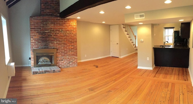 unfurnished living room with sink, light hardwood / wood-style flooring, beamed ceiling, and a brick fireplace