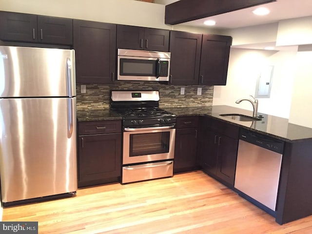 kitchen featuring dark stone counters, sink, stainless steel appliances, and light hardwood / wood-style flooring