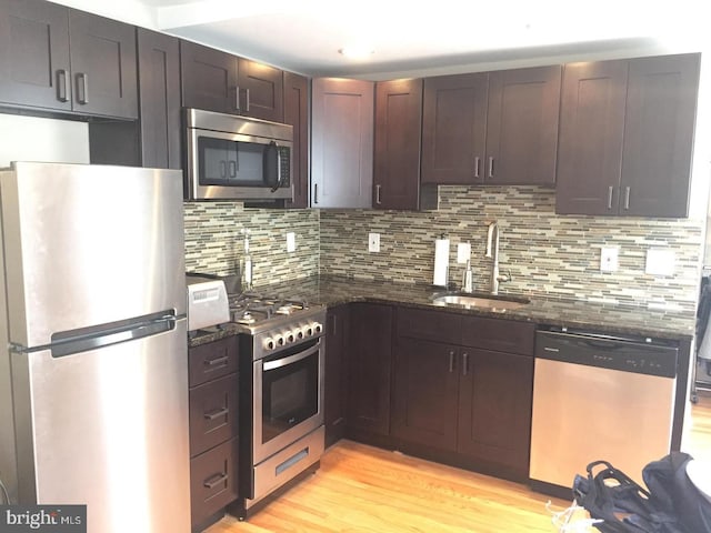 kitchen with sink, light hardwood / wood-style flooring, dark stone countertops, appliances with stainless steel finishes, and tasteful backsplash