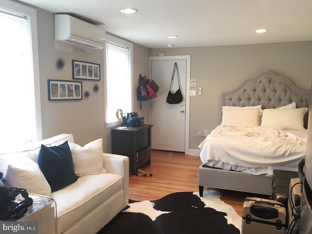 bedroom featuring multiple windows, a wall mounted AC, and light wood-type flooring