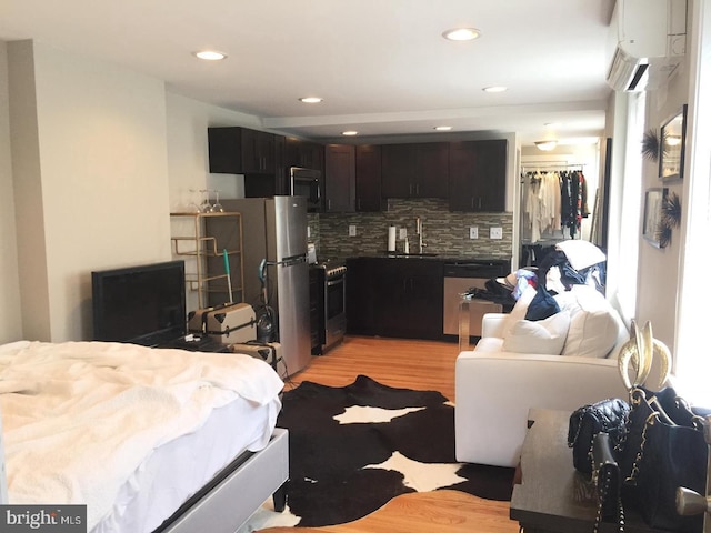 bedroom with stainless steel fridge, light wood-type flooring, a wall mounted AC, sink, and a closet