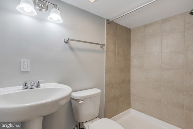 bathroom with tiled shower, toilet, and sink