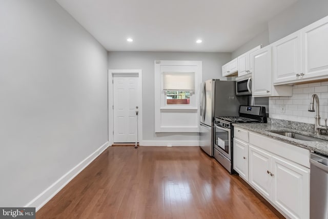 kitchen featuring light stone counters, stainless steel appliances, sink, wood-type flooring, and white cabinets